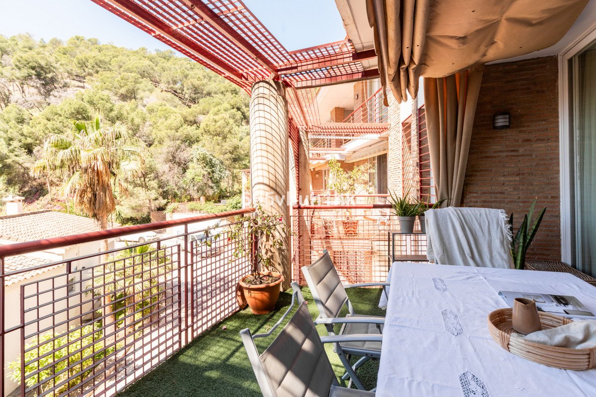 A covered balcony with a table, chairs, plants, and a view of trees and buildings.