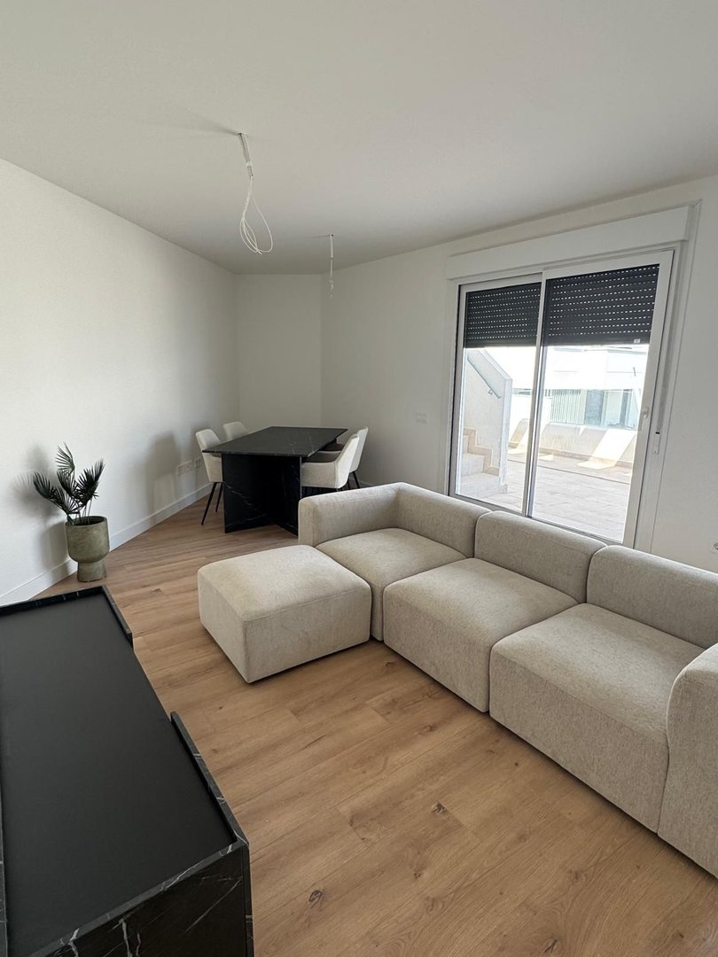 Modern living and dining area with a sectional sofa, ottoman, dark dining table, and sliding glass doors leading outside.