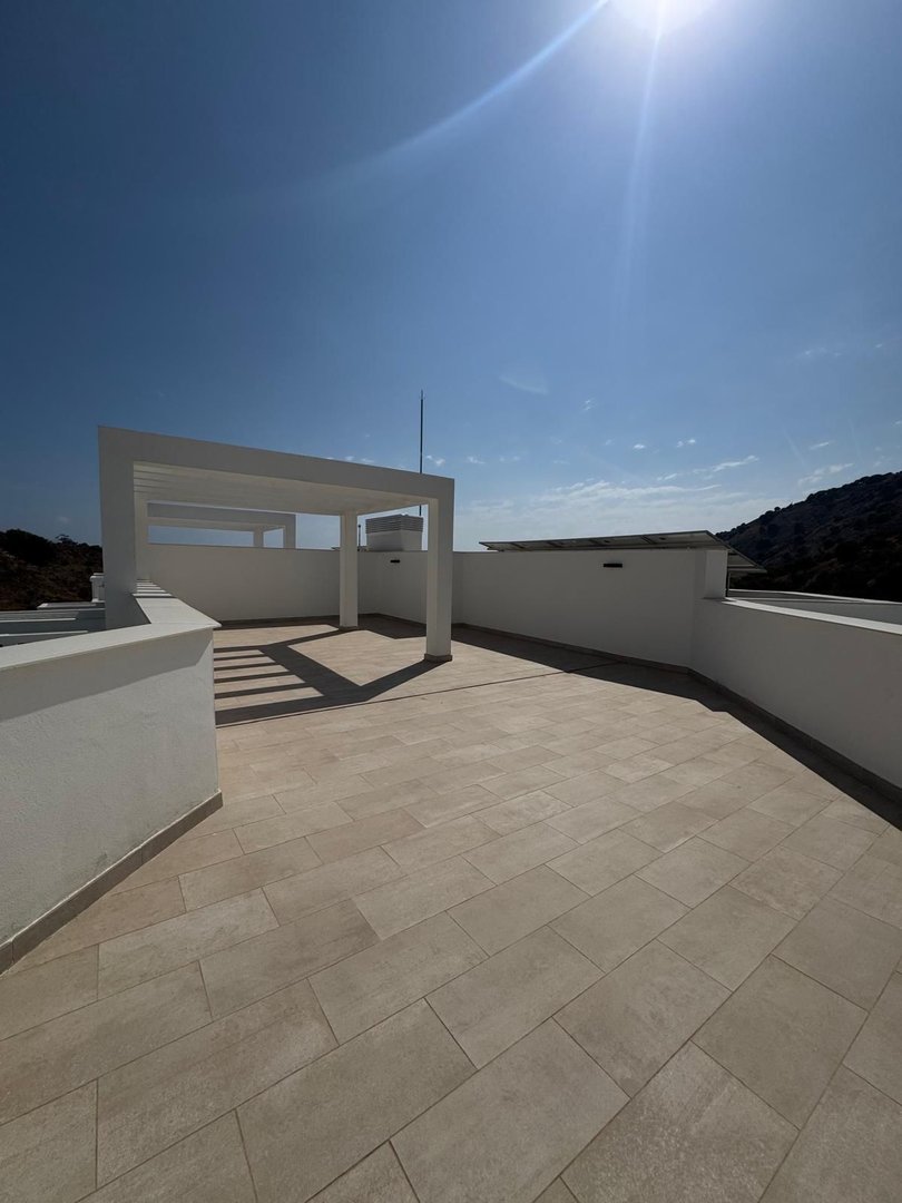 A modern terrace with a white pergola and tiled flooring, offering a spacious outdoor area with a scenic view under a bright sky.
