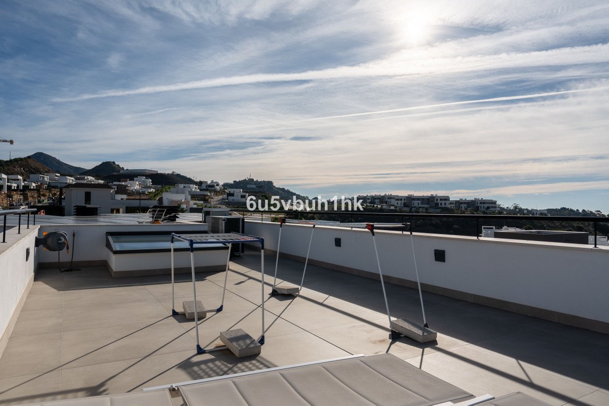 A spacious terrace with a small jacuzzi, lounge chairs, and a clear view of distant buildings and hills under a cloudy sky.