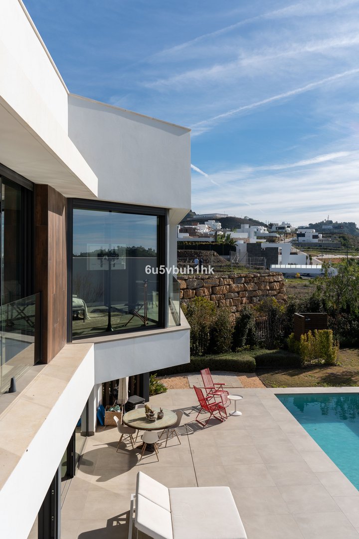 Modern villa with swimming pool, terrace furniture, and scenic hillside view of white houses under a blue sky with clouds.