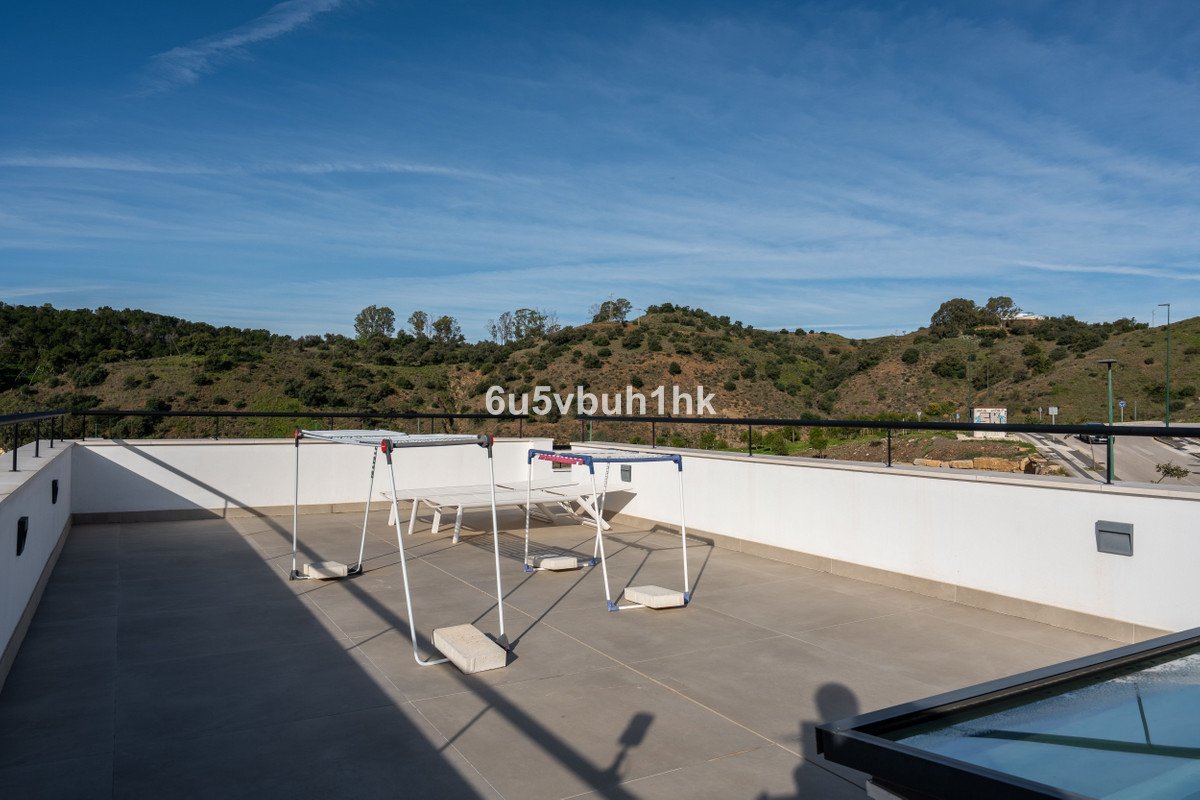 Spacious terrace with a white table and chairs, overlooking green hills under a blue sky.