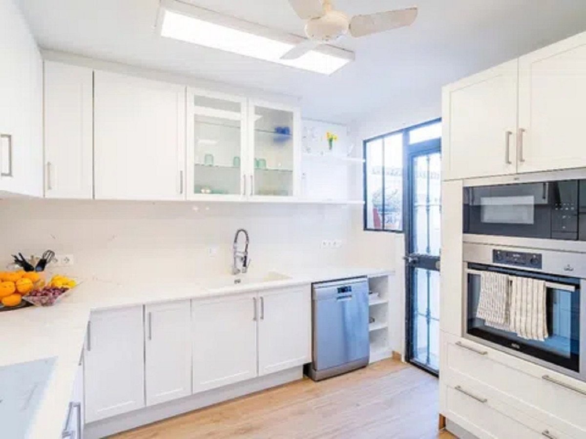 Modern white kitchen with stainless steel appliances, a dishwasher, and a glass door leading outside.