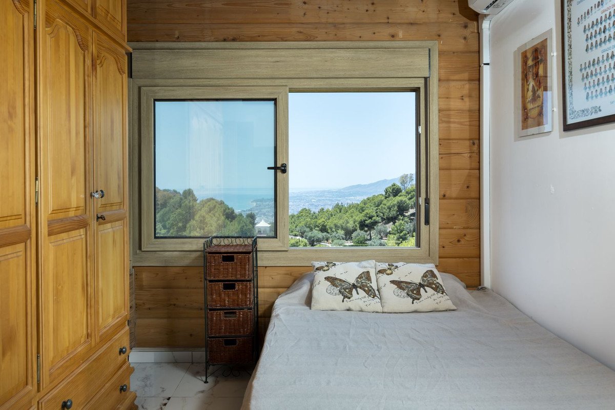 Cozy bedroom with wooden walls, a bed, and a window showing sea and mountain views.