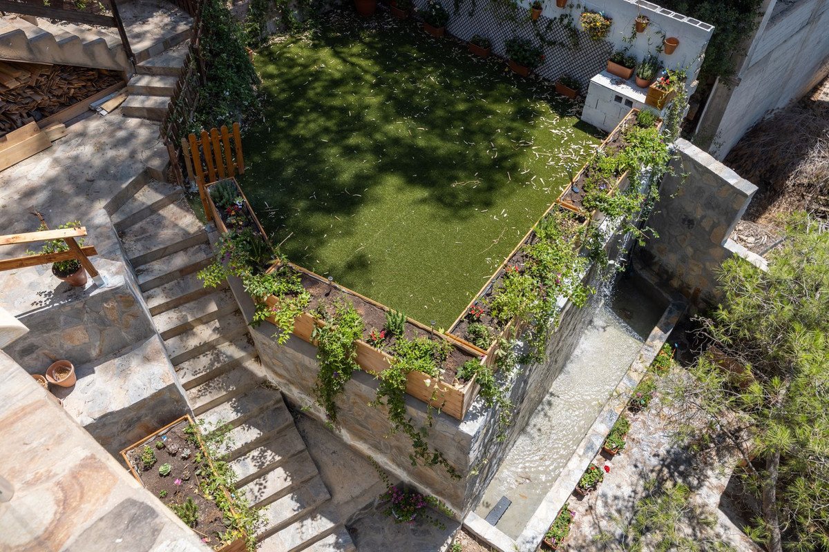 Rooftop garden with stone stairs, green lawn, and wooden planters with climbing plants.