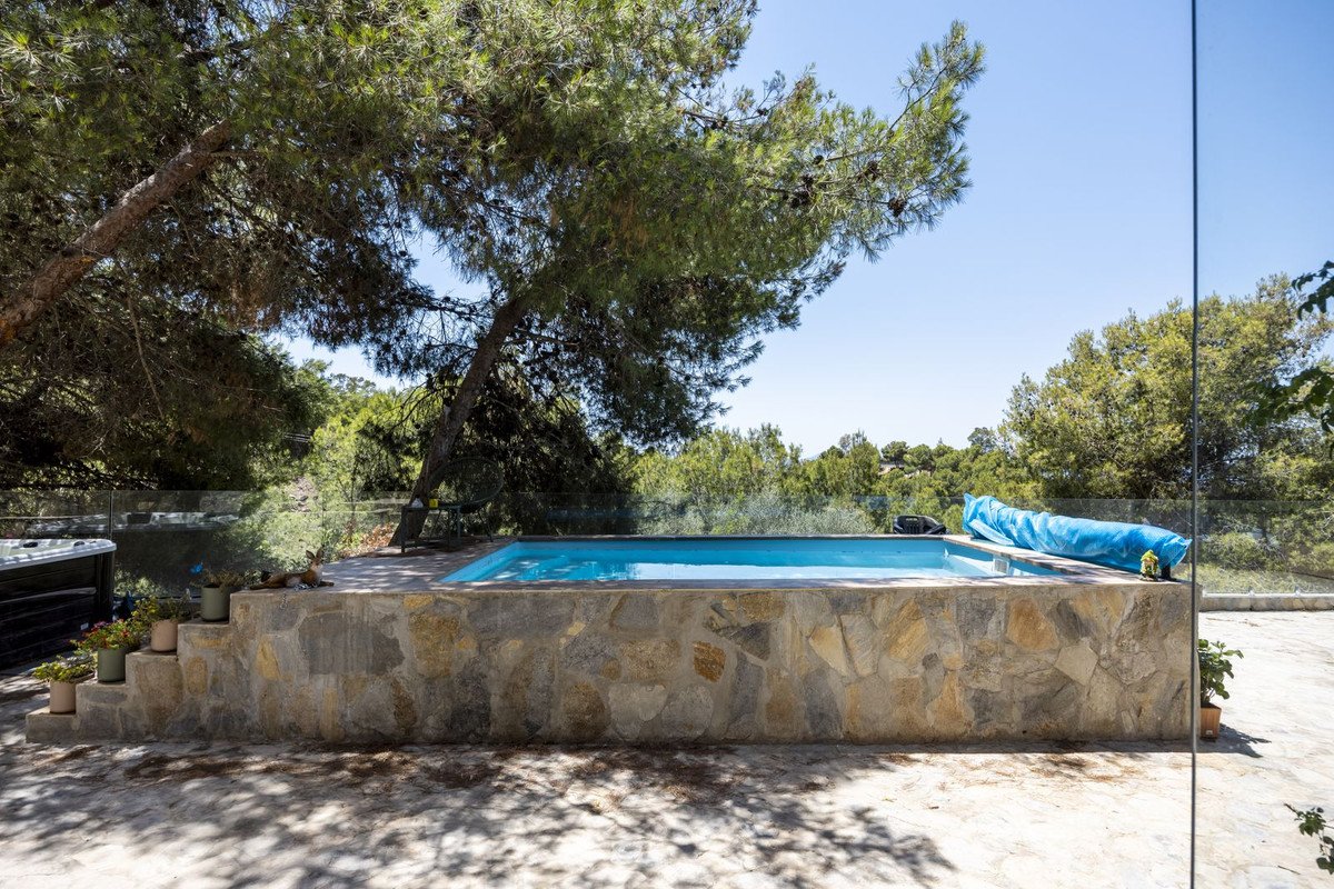 Outdoor swimming pool with stone terrace, surrounded by trees and clear blue sky.