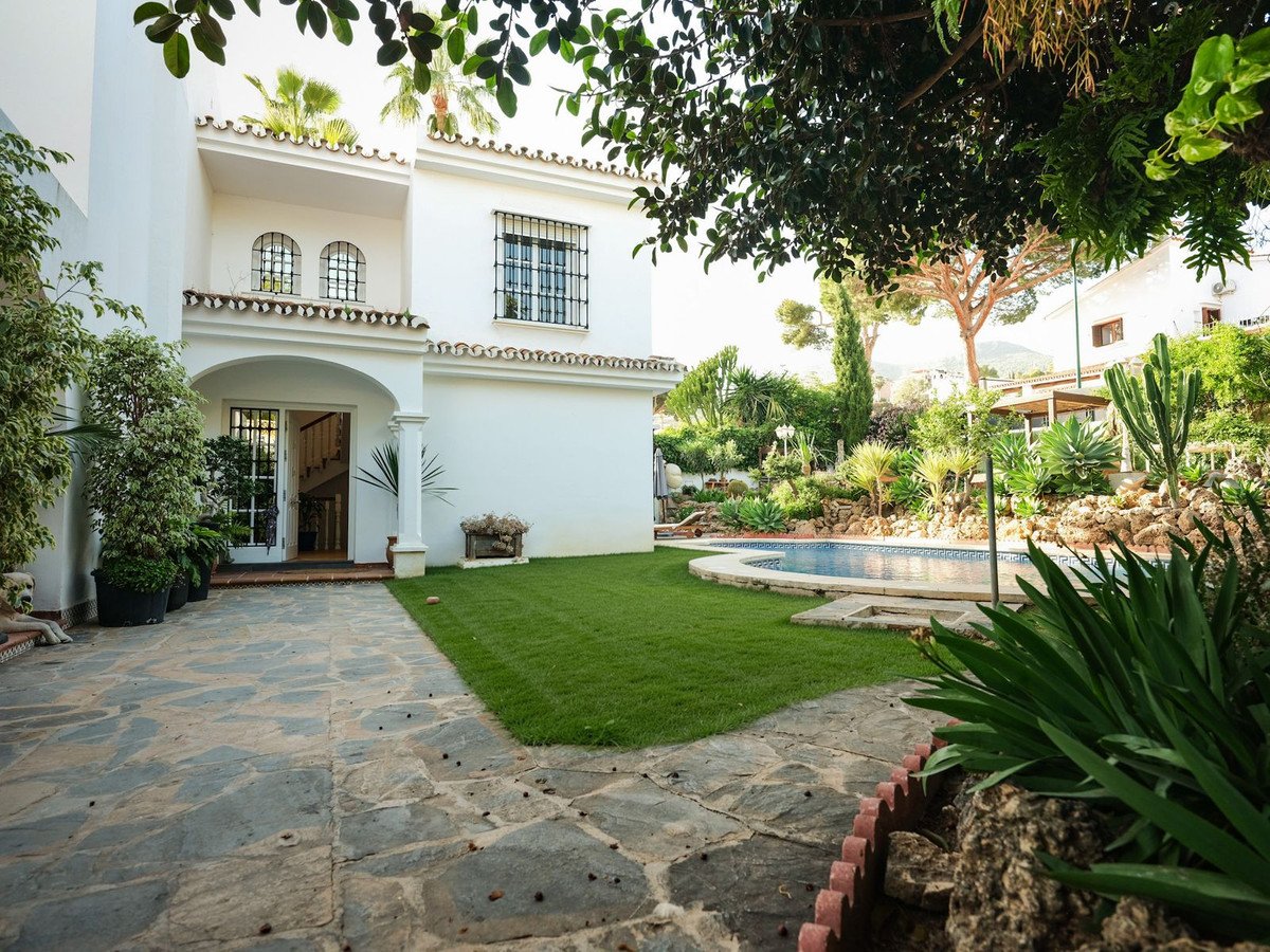 A white villa with a swimming pool and a lush garden, featuring a stone pathway and green lawn.