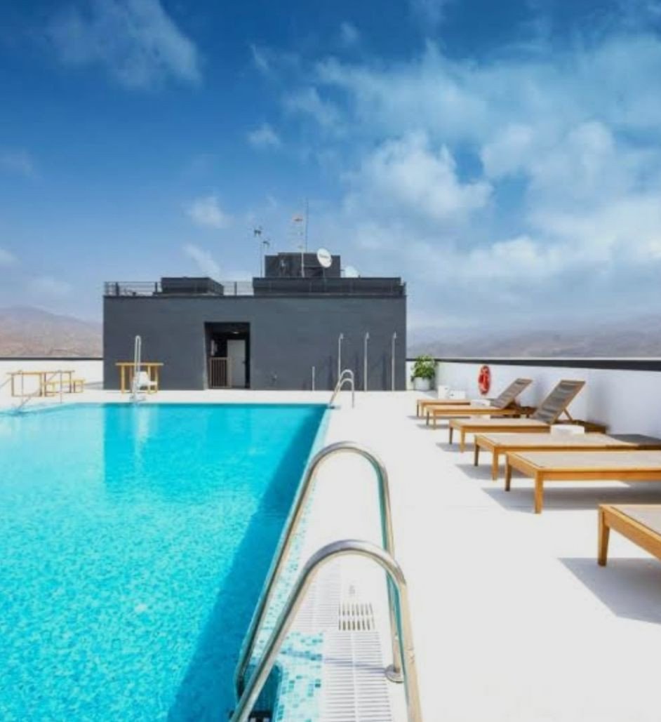 A rooftop swimming pool with lounge chairs and a view of the blue sky and distant hills.