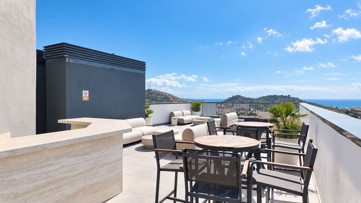 Modern rooftop terrace with lounge seating, dining tables, bar, and panoramic sea and mountain views.