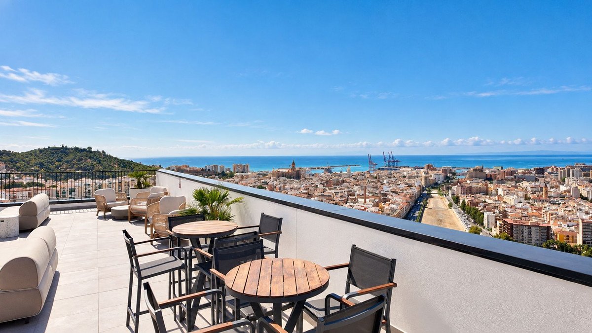 A spacious terrace with seating areas and tables, offering panoramic views of the city and the sea under a clear blue sky.