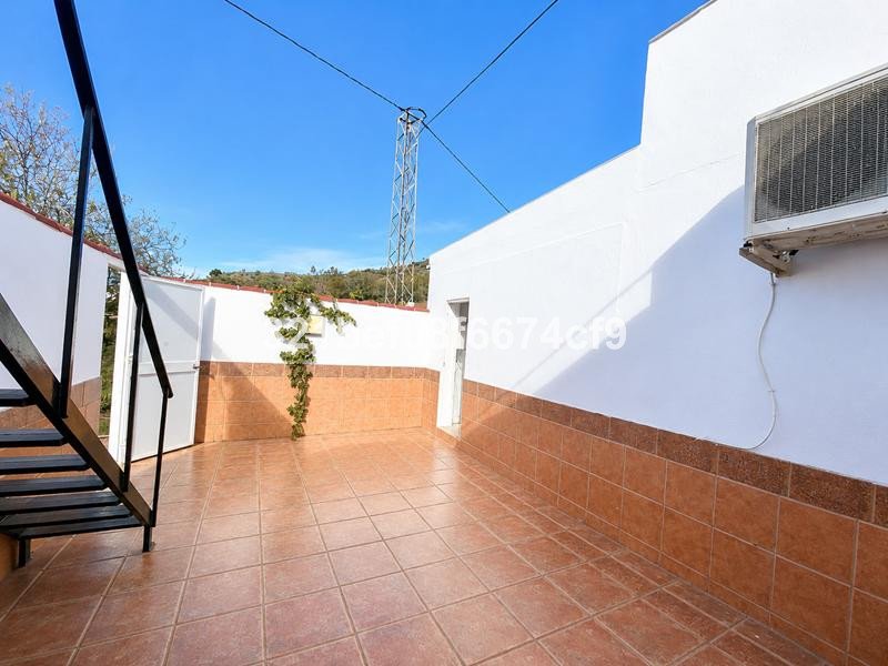 A tiled terrace with a metal staircase leading up, overlooking a green hillside under a clear blue sky.