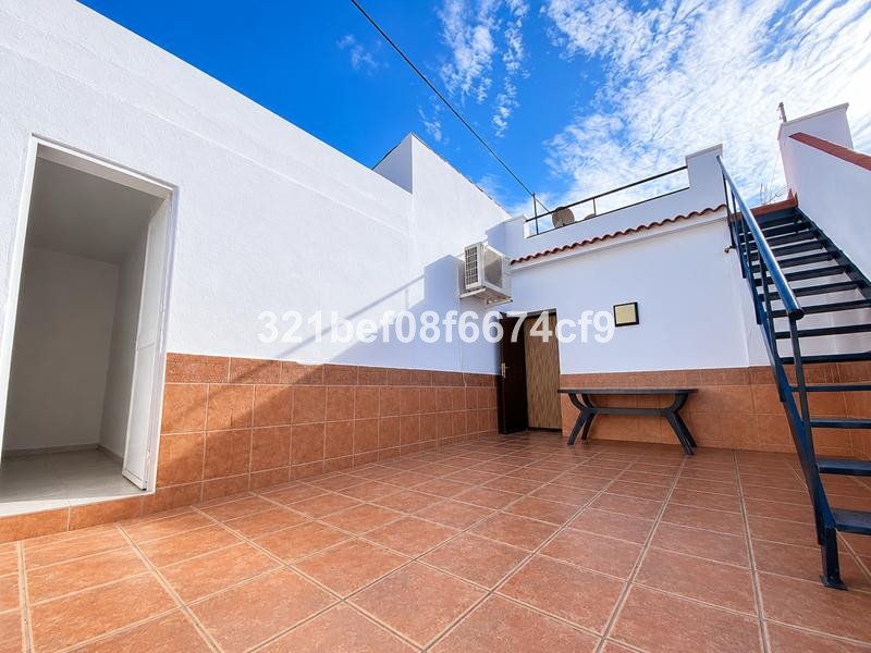 An outdoor tiled terrace with a bench, stairs leading up to a rooftop, and an air conditioning unit on the wall.