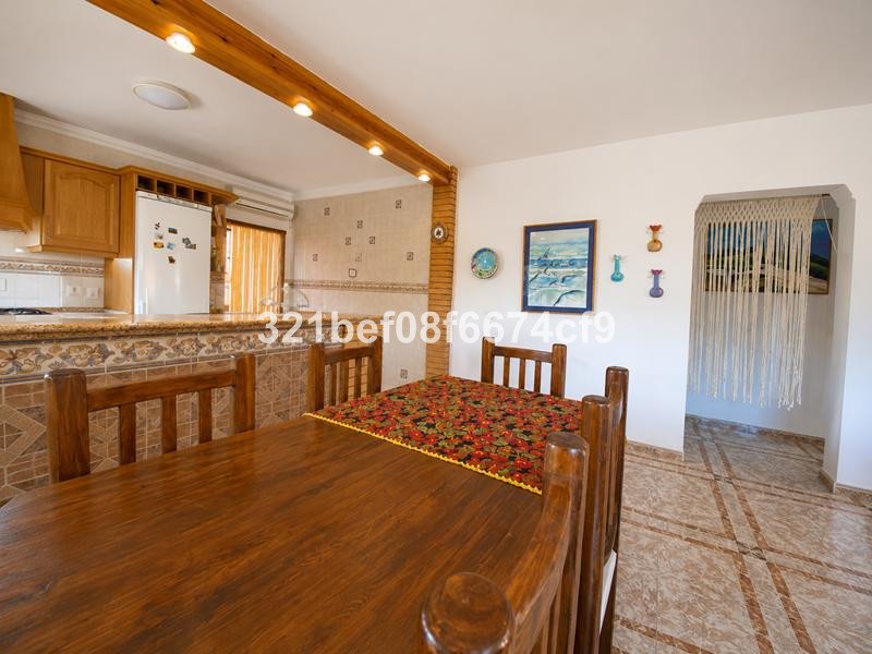 Wooden dining table and chairs in front of a kitchen area with wooden cabinets and a refrigerator.