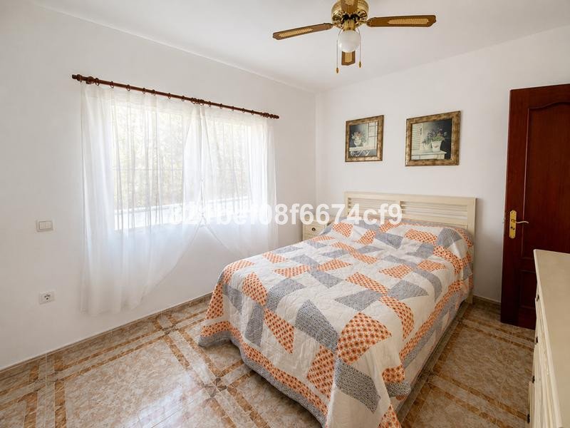 A bedroom with a double bed, patterned quilt, white curtains, and two framed pictures on the wall.