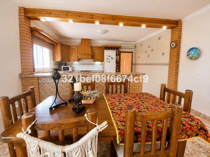 Open-concept dining and kitchen area with a wooden table, chairs, and rustic wooden cabinets.