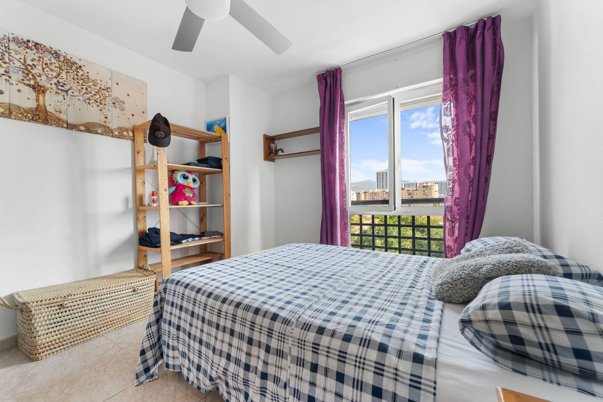 Gemütliches Schlafzimmer mit Stadtblick, kariertem Überwurf, Holzregalen und großem Fenster mit lila Vorhängen.