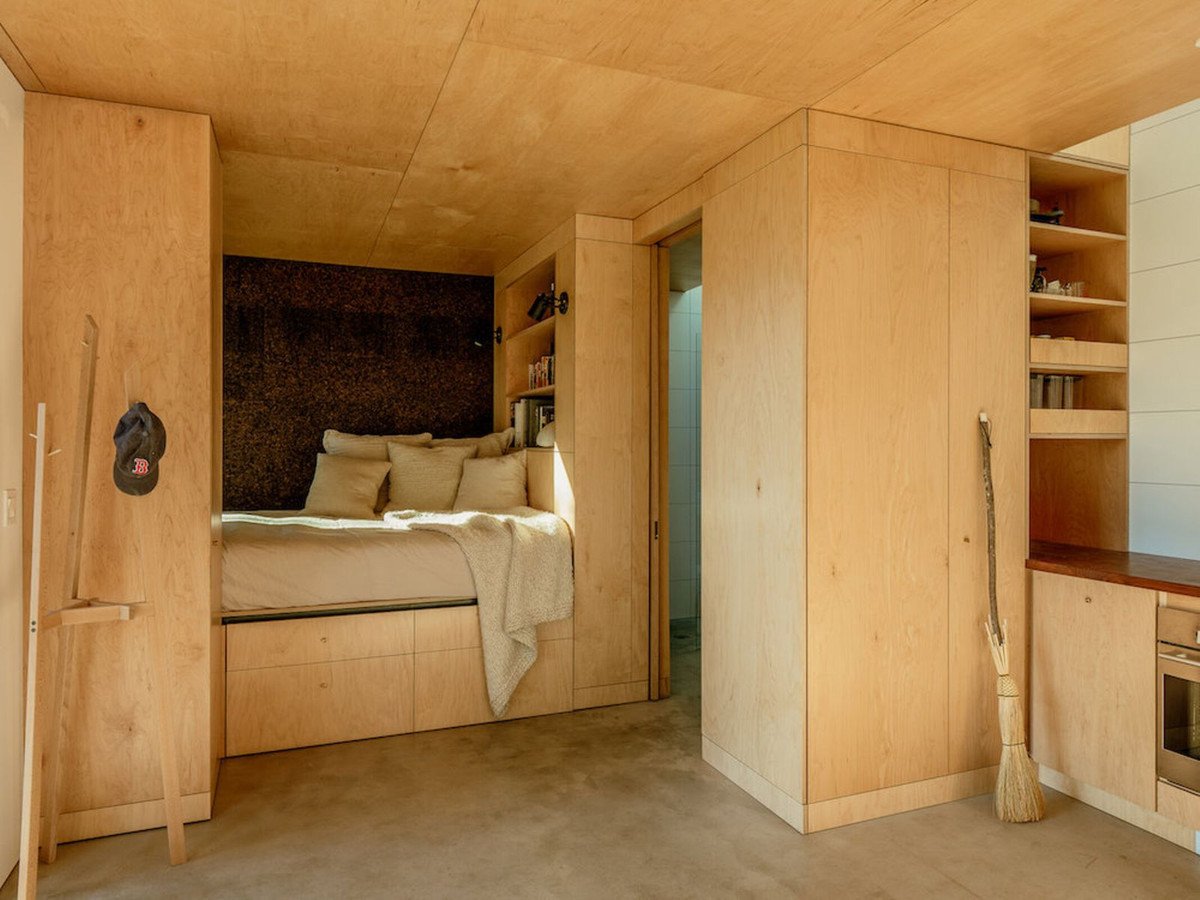 Houten slaapkamer met bed, planken en hoed aan de muur.
