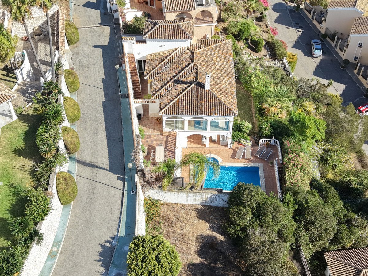 Aerial view of a luxurious villa with a private swimming pool, sun loungers, and a beautiful garden, offering scenic views.