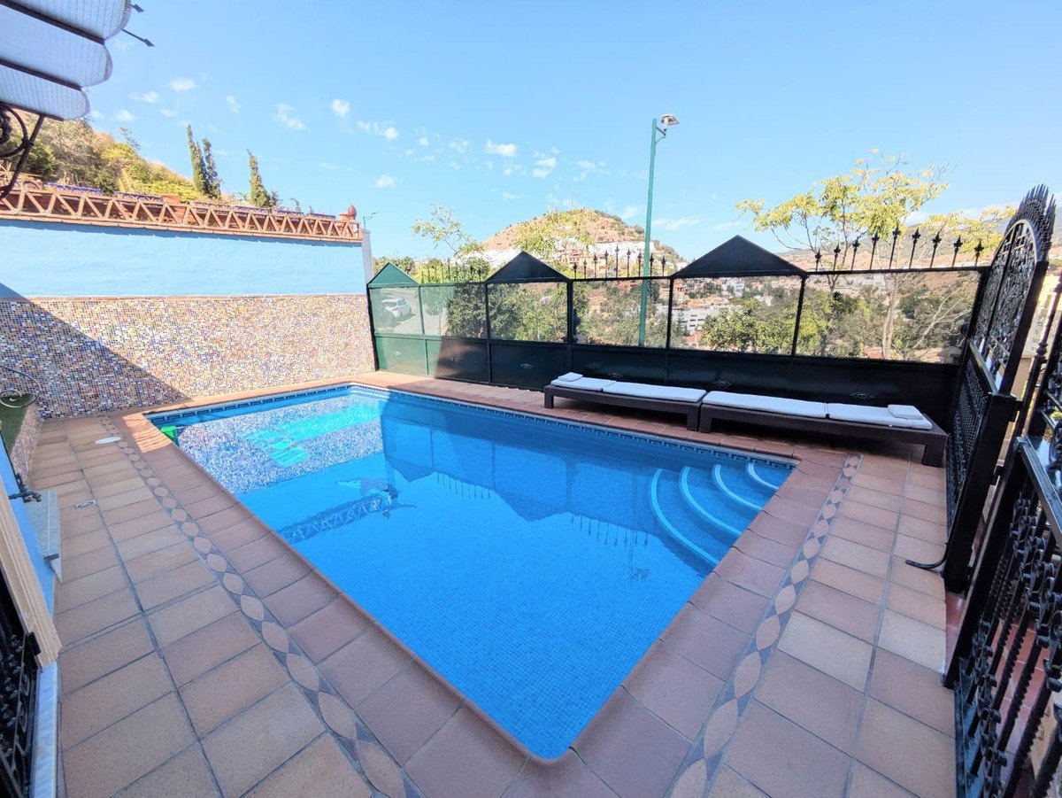 Outdoor pool with clear blue water, surrounded by tiled deck and lounge chairs, scenic hillside view.