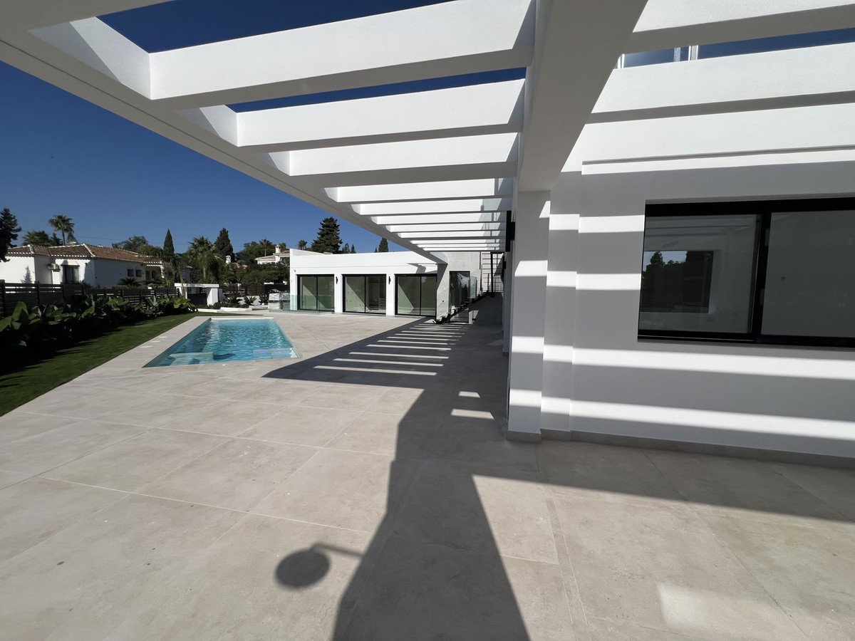 Modern white villa with a rectangular swimming pool and spacious patio area, offering a bright and airy outdoor living space.