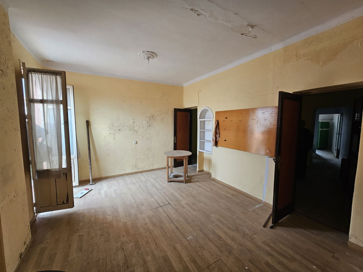 Lege kamer met houten vloer, gele muren en klein rond tafeltje.
