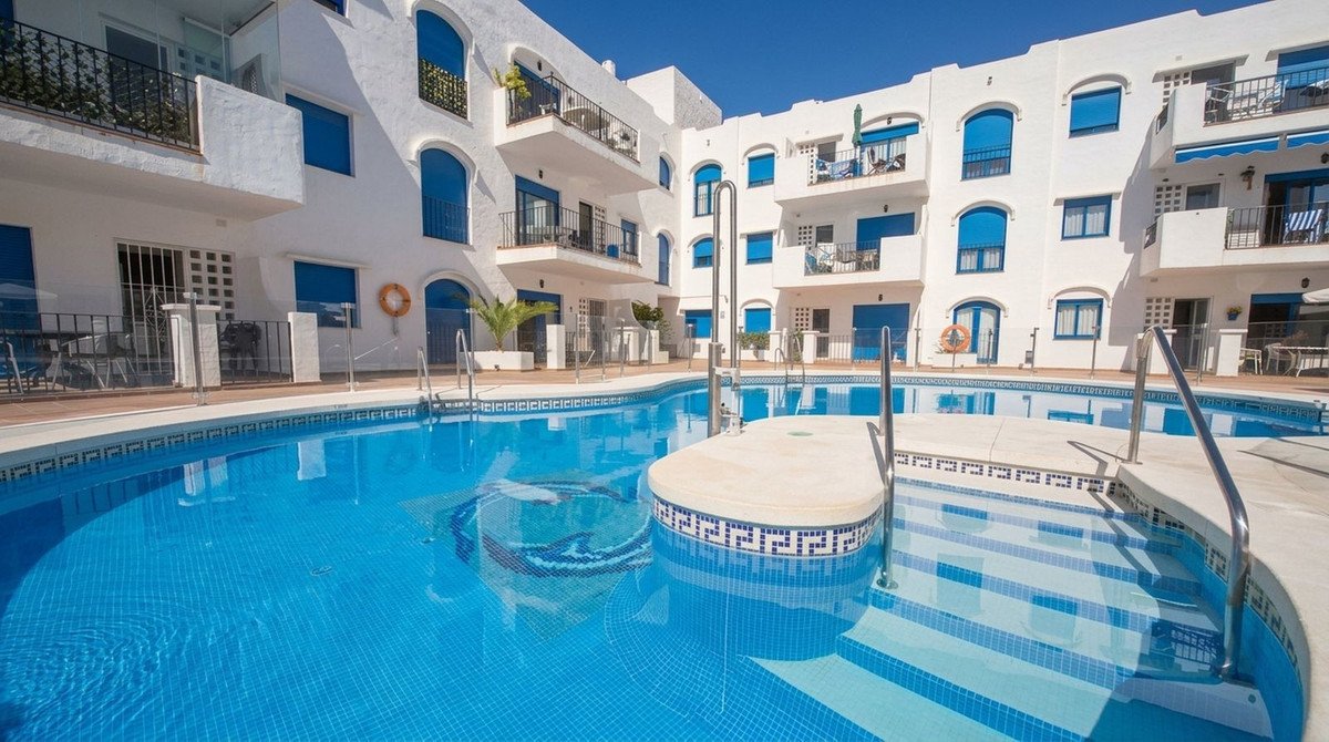 Resort complex with a large blue swimming pool and steps, surrounded by white buildings with blue windows.