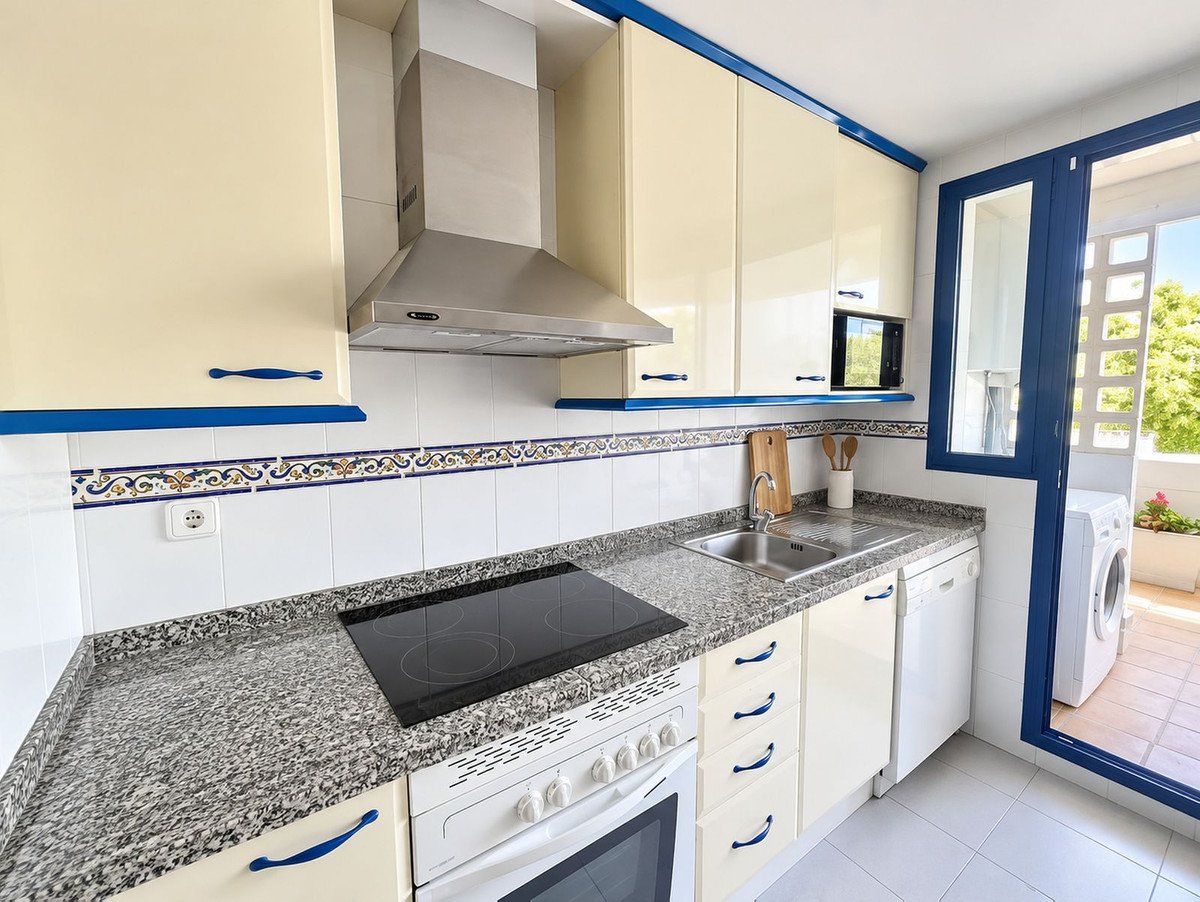Modern kitchen with cream cabinets, granite countertops, stainless steel appliances, and a view of the balcony with a washing machine.