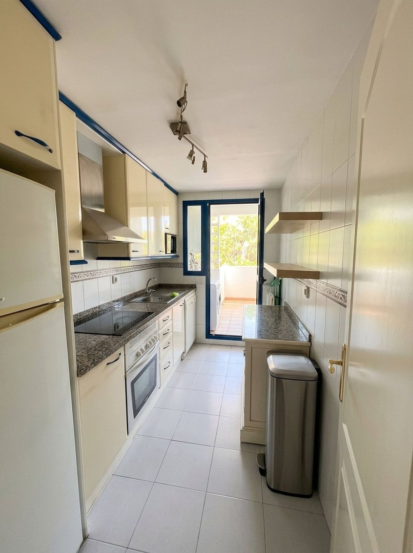 A compact kitchen with cream cabinets, granite countertops, oven, and direct access to a sunny balcony with a washing machine.