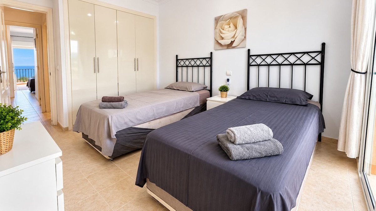 Bedroom with two twin beds, large wardrobe, and a hallway leading to a balcony with a sea view.