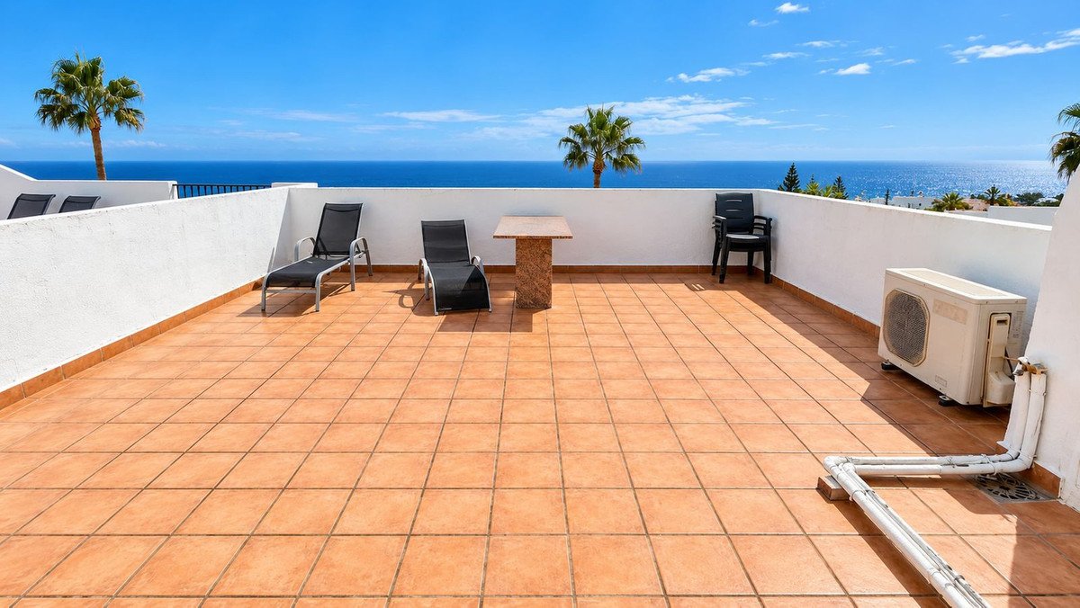 Spacious tiled terrace with lounge chairs, a small table, air conditioning unit, and a beautiful blue sea view under a clear sky.