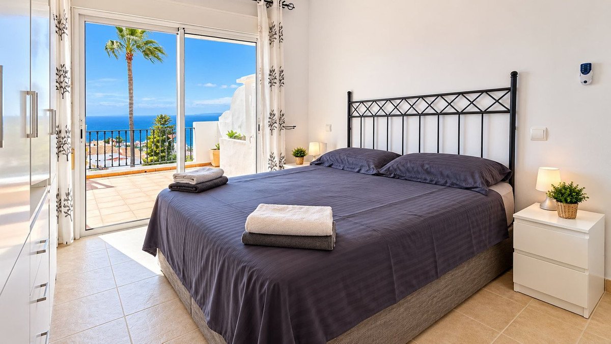 Bedroom with a large bed and ocean views from the balcony, featuring a palm tree and coastal scenery.