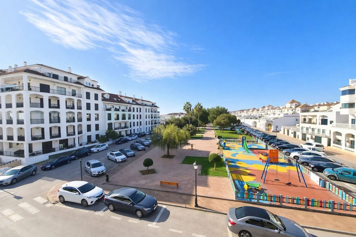 Apartment buildings overlook a colorful playground and a street lined with parked cars.