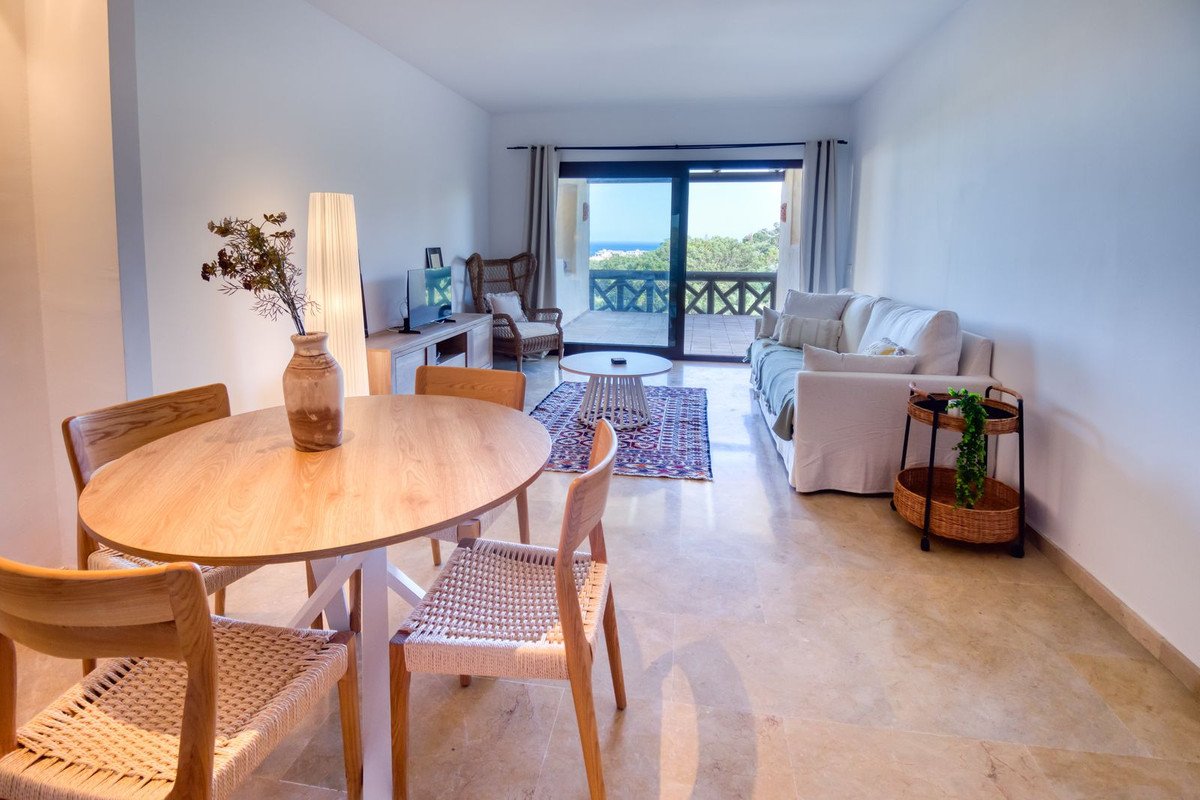 Modern living and dining area with a balcony offering a beautiful sea view and lush green trees.