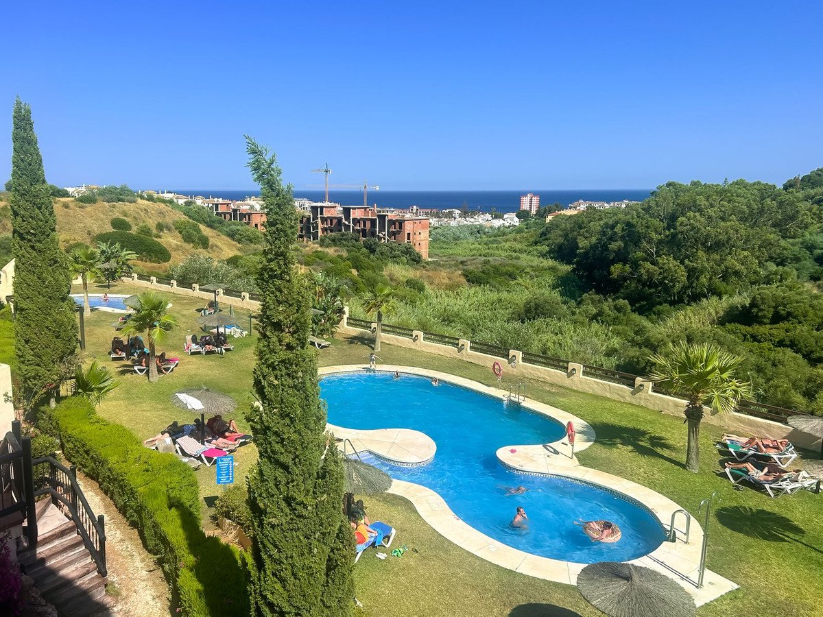 Resort pool area with lounge chairs and umbrellas, overlooking lush greenery and the sea.