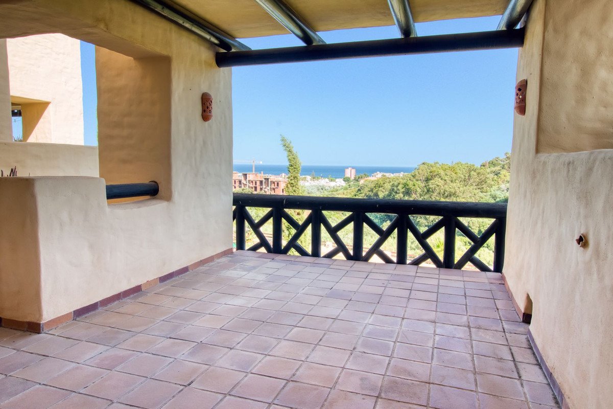 Terrace with a view of the sea and distant buildings, surrounded by green trees and a clear blue sky.