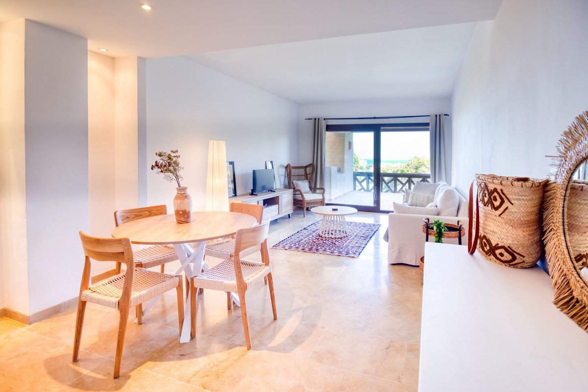Bright open-plan living and dining area with a balcony overlooking the sea and lush greenery.