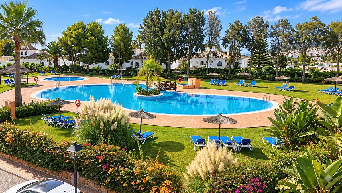 A large resort pool surrounded by green grass, lounge chairs, umbrellas, and palm trees under a clear blue sky.