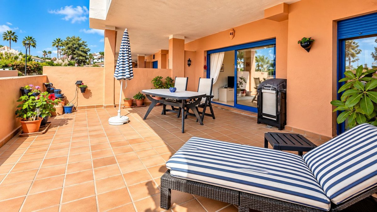 Spacious terrace with dining set, sun lounger, barbecue, and potted plants, offering a view of palm trees and houses.