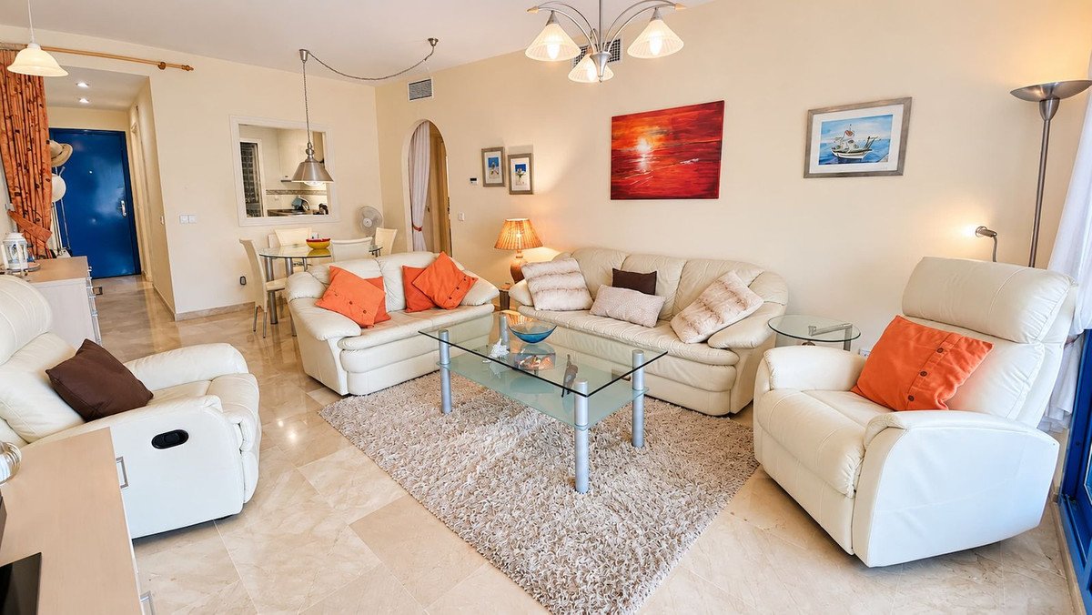 Modern living room with white leather sofas, glass coffee table, and view of a dining area through an archway.