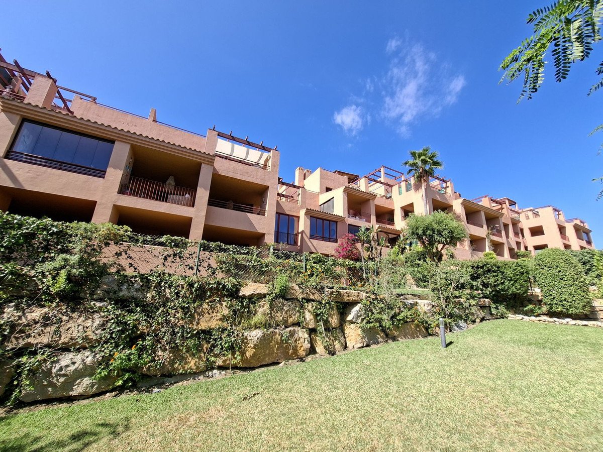 Modern terraced apartments with balconies and large windows, set against a clear blue sky, surrounded by lush greenery.