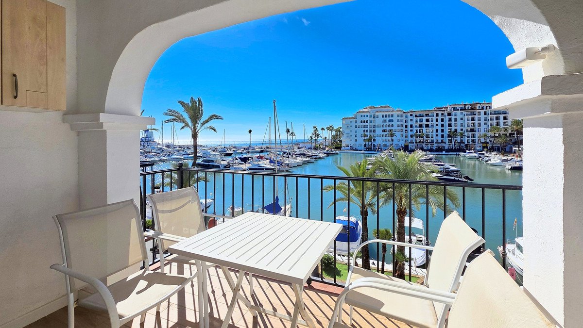 Balcony with table and chairs overlooking a marina with boats and palm trees
