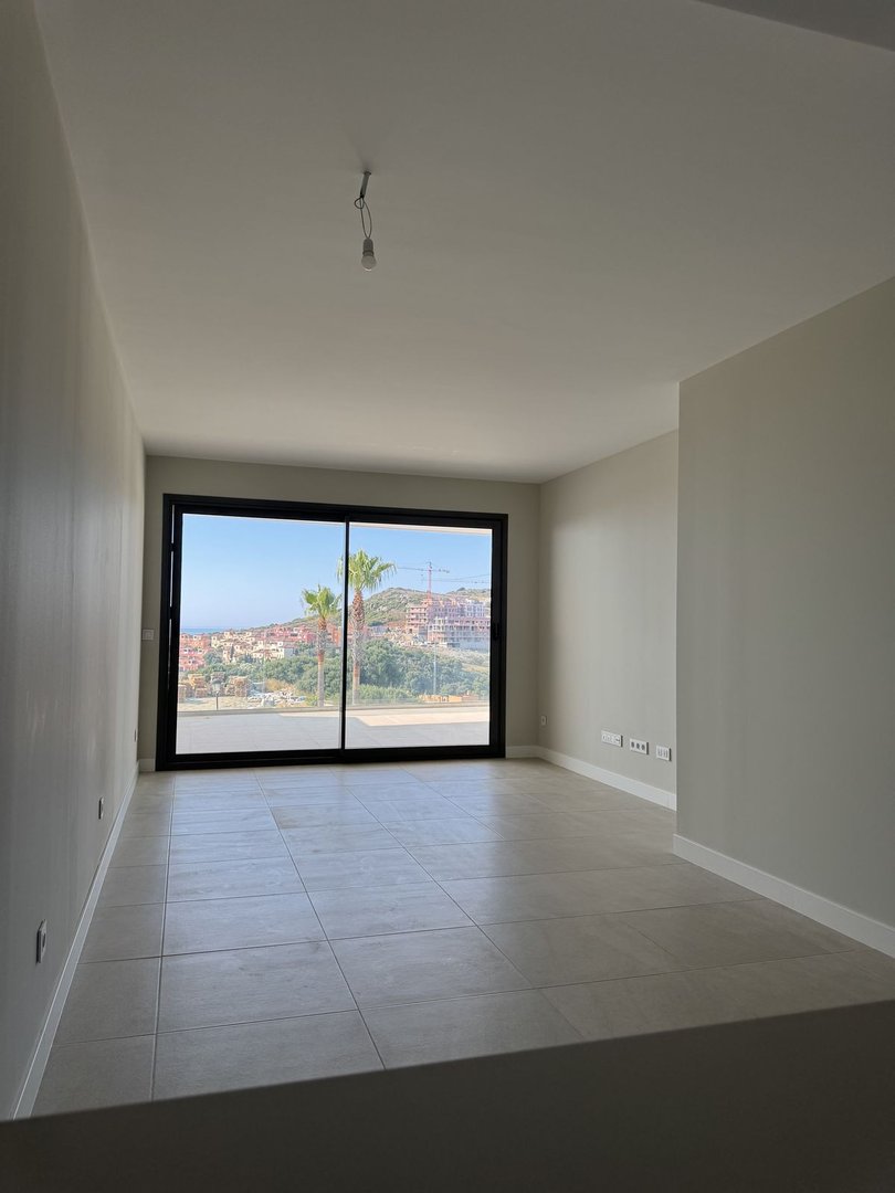 Spacious living room with large sliding doors offering a sea view, palm trees, and a distant town.