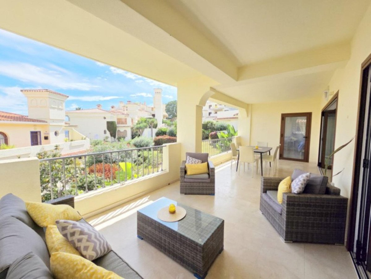 Spacious terrace with outdoor seating, coffee table, and a view of Mediterranean-style buildings and lush greenery.