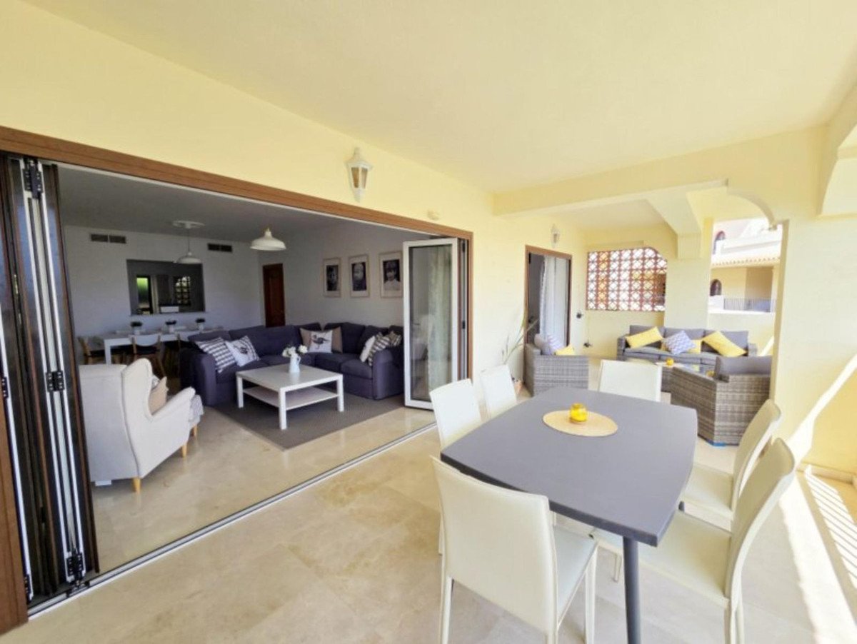 Spacious open-plan living area with comfortable sofas, dining table on a terrace with outdoor seating, and a glimpse of the interior.