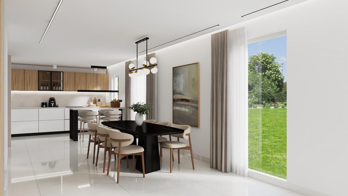 Modern dining area and kitchen with island, overlooking a lush green garden through large windows.
