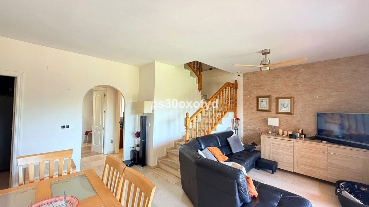 Spacious living room with black leather sofas, a wooden staircase, dining area, and a television console.