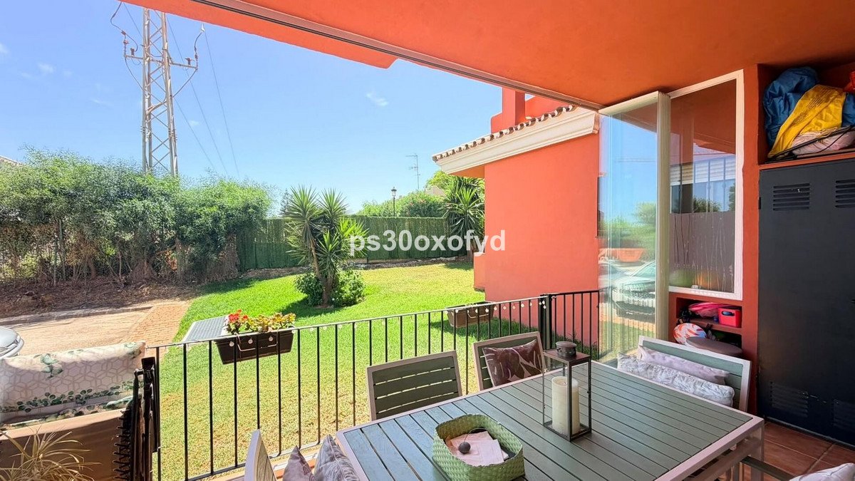 Terrace with a table and chairs overlooking a green garden and blue sky on a sunny day.