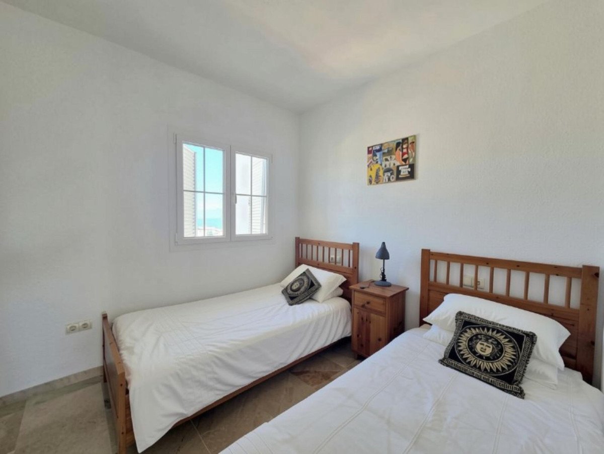 A bedroom with two twin beds, white linens, and a window offering a view of the sea and cityscape.