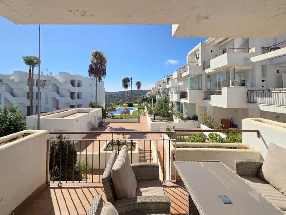 Terrace view of white apartment buildings with a swimming pool and palm trees under a clear blue sky.