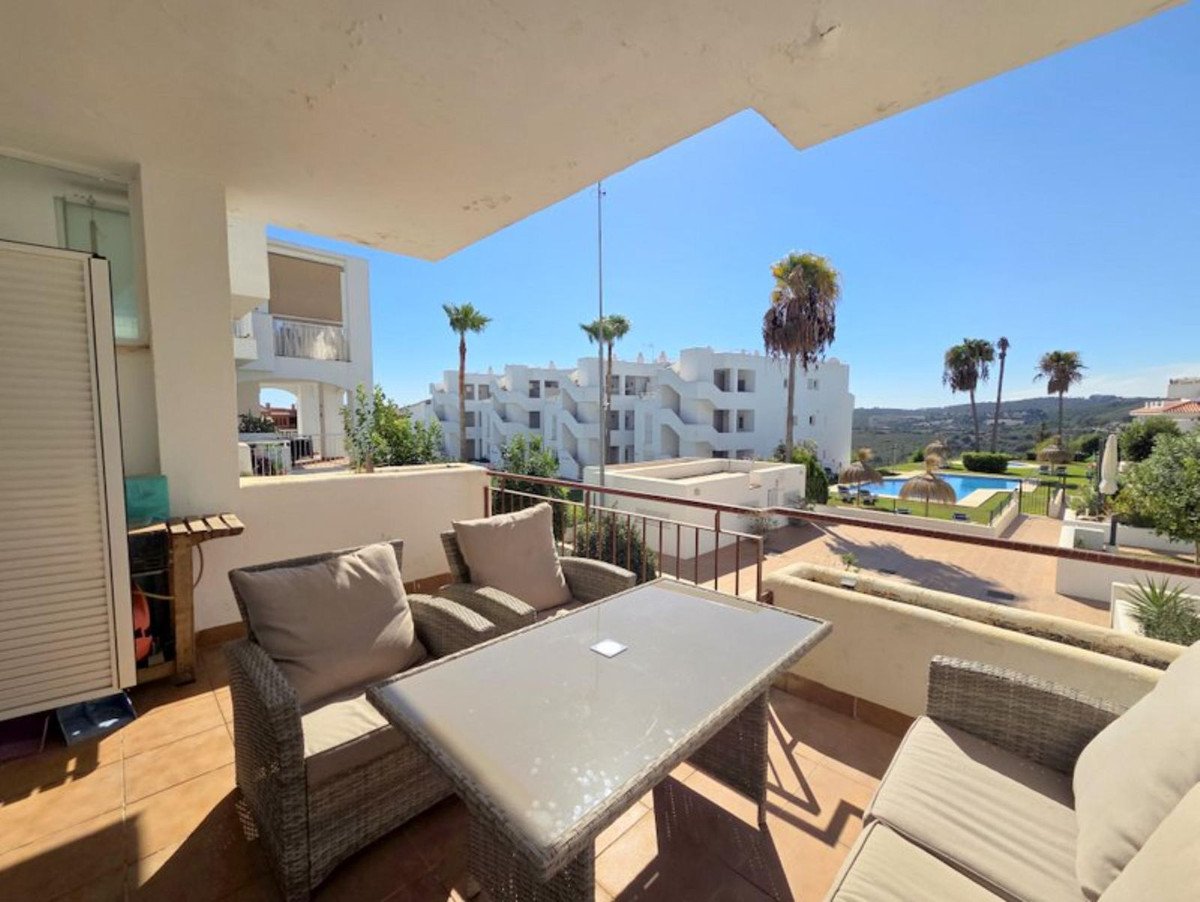Terrace with seating and table overlooking a swimming pool and palm trees on a sunny day.